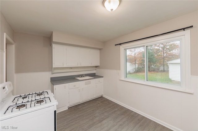 kitchen featuring white range with gas stovetop, sink, hardwood / wood-style floors, and white cabinets