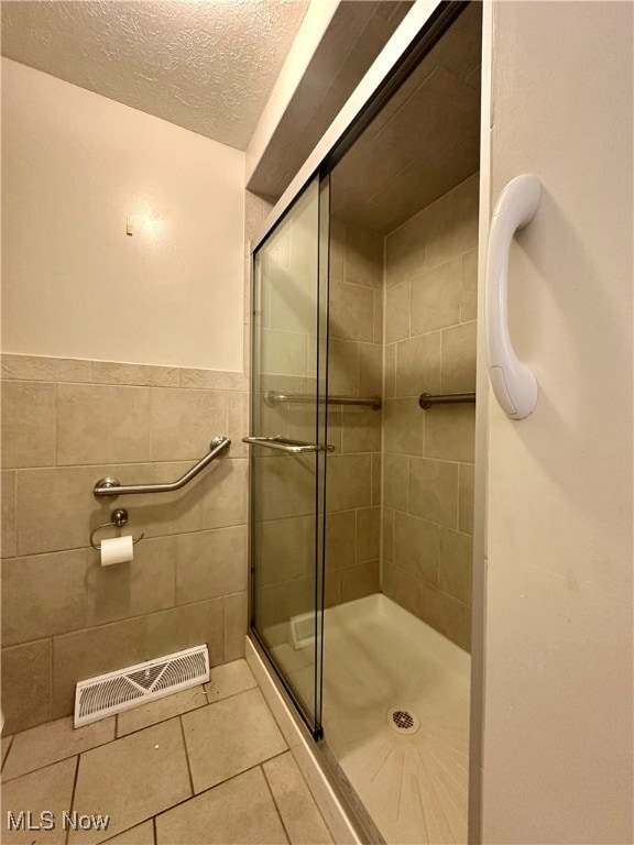 bathroom featuring tile walls, a textured ceiling, tile patterned floors, and a shower with door