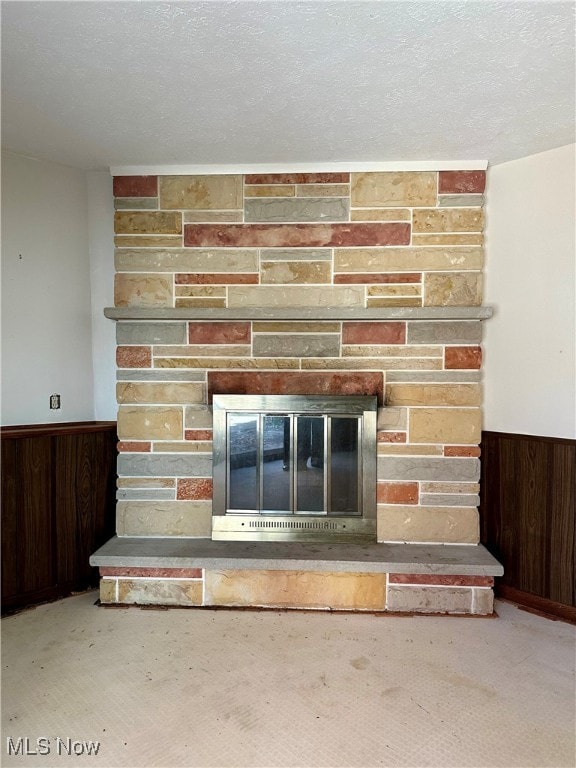 room details with a stone fireplace, carpet, wood walls, and a textured ceiling