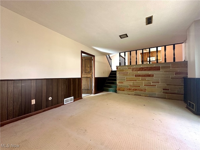 carpeted spare room with a textured ceiling and wooden walls