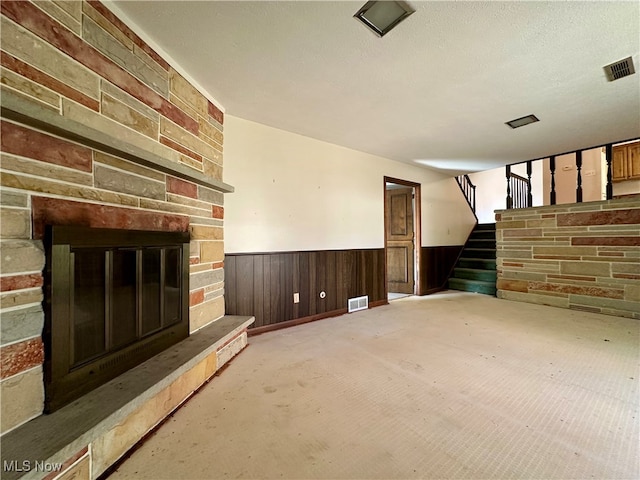 unfurnished living room featuring a stone fireplace, wooden walls, and a textured ceiling