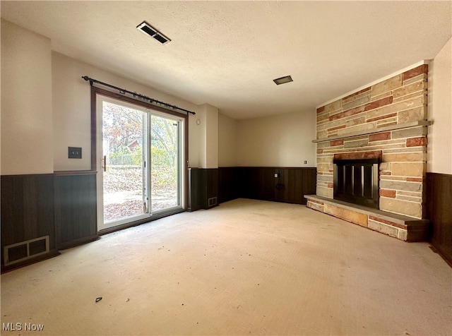 unfurnished living room featuring wood walls, a stone fireplace, and a textured ceiling