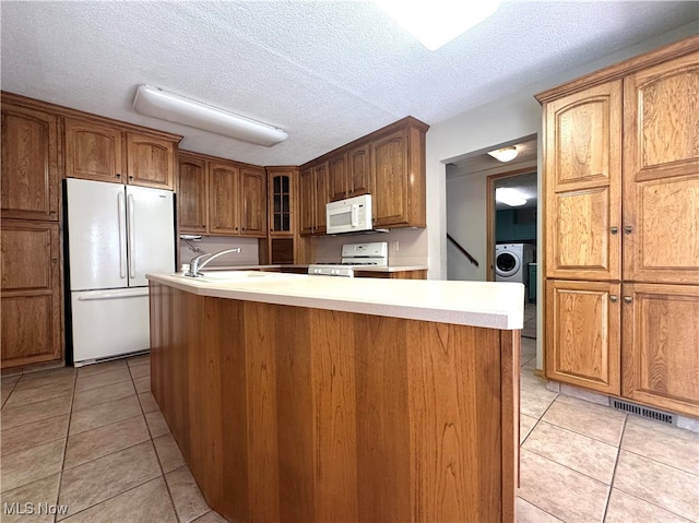 kitchen with washer / clothes dryer, white appliances, light tile patterned floors, and a center island with sink