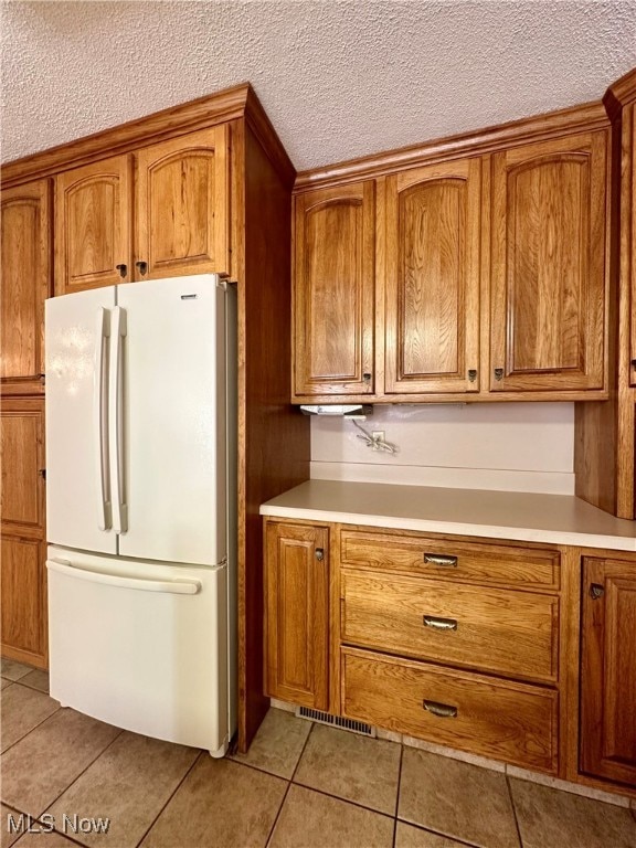 kitchen featuring white refrigerator, a textured ceiling, and light tile patterned flooring