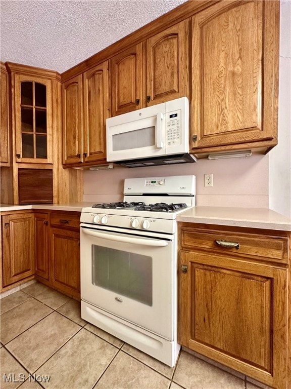 kitchen featuring white appliances, a textured ceiling, and light tile patterned floors