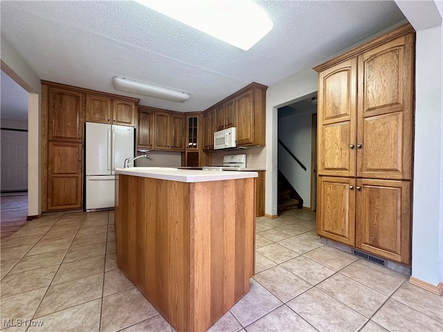 kitchen featuring a textured ceiling, light tile patterned floors, white appliances, and an island with sink