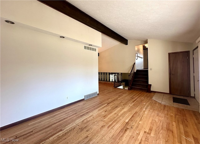 unfurnished living room featuring a textured ceiling, light hardwood / wood-style floors, and vaulted ceiling with beams