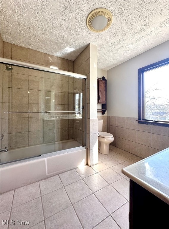 full bathroom featuring tile patterned flooring, a textured ceiling, vanity, toilet, and tile walls