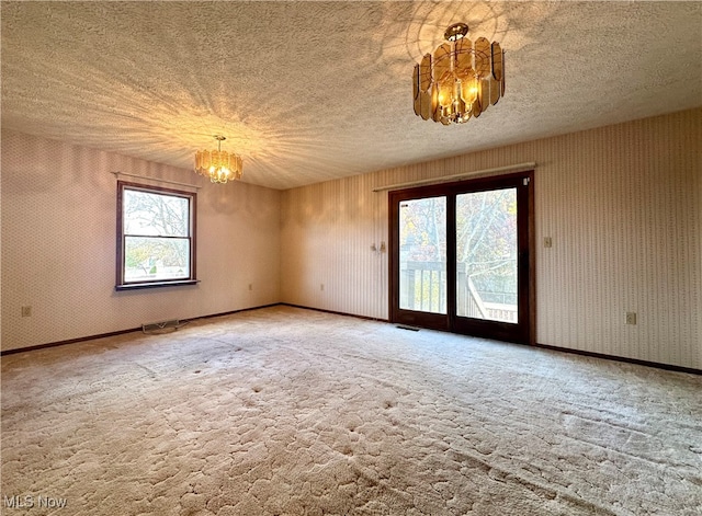 carpeted empty room with a notable chandelier and a textured ceiling