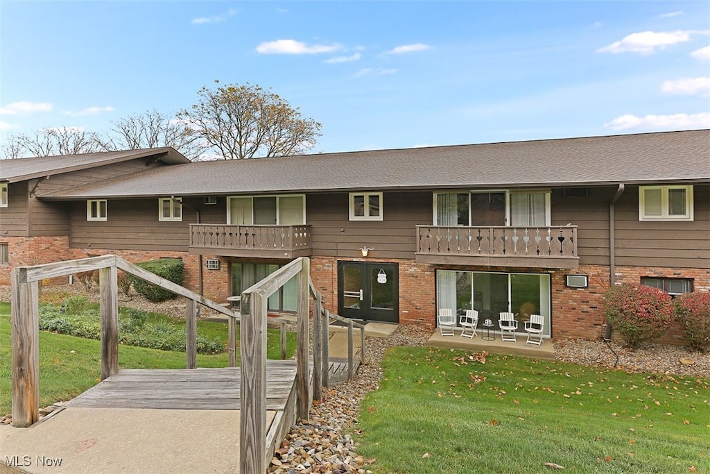 rear view of property featuring a patio, a yard, and a balcony