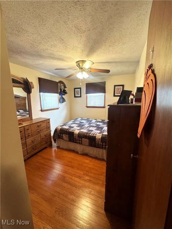 bedroom with hardwood / wood-style floors, ceiling fan, and a textured ceiling