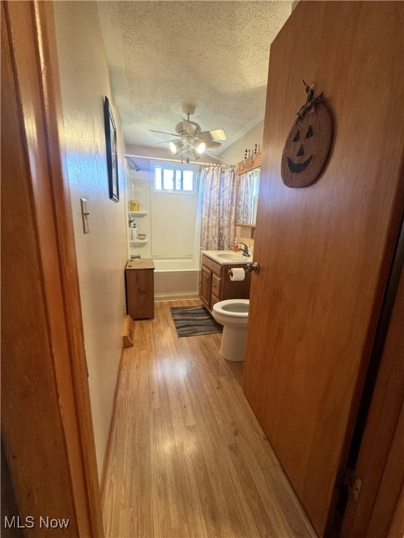 full bathroom featuring hardwood / wood-style flooring, ceiling fan, a textured ceiling, shower / tub combo with curtain, and toilet