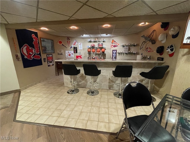 bar with a drop ceiling and wood-type flooring