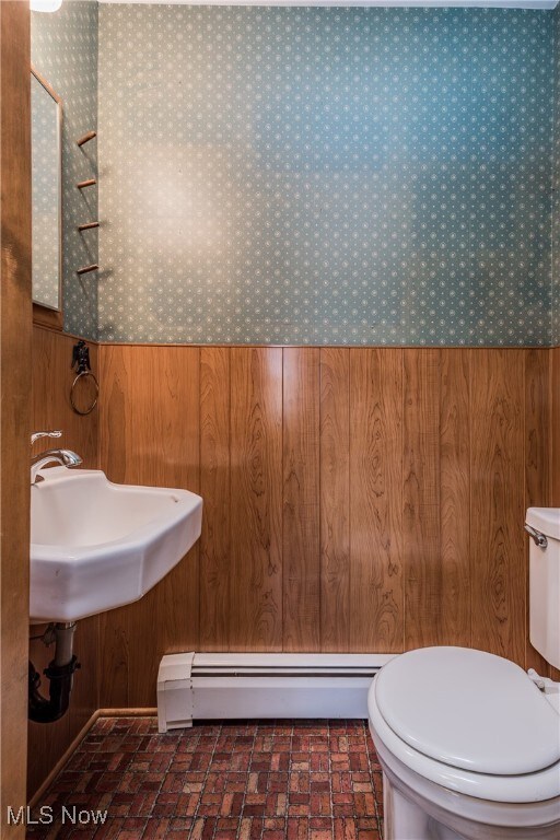 bathroom featuring sink, a baseboard radiator, wooden walls, and toilet