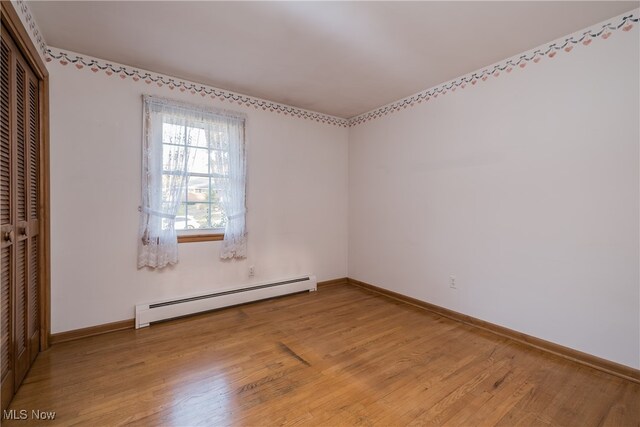 unfurnished room with wood-type flooring and a baseboard heating unit