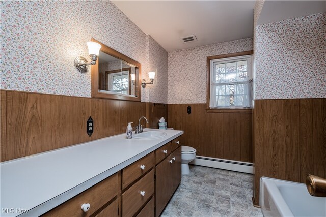 bathroom featuring a baseboard radiator, toilet, wooden walls, vanity, and a tub to relax in