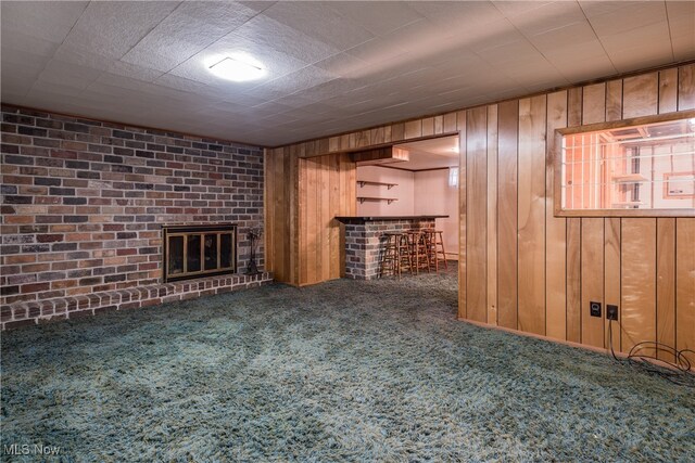 unfurnished living room with carpet, a fireplace, bar area, wood walls, and brick wall