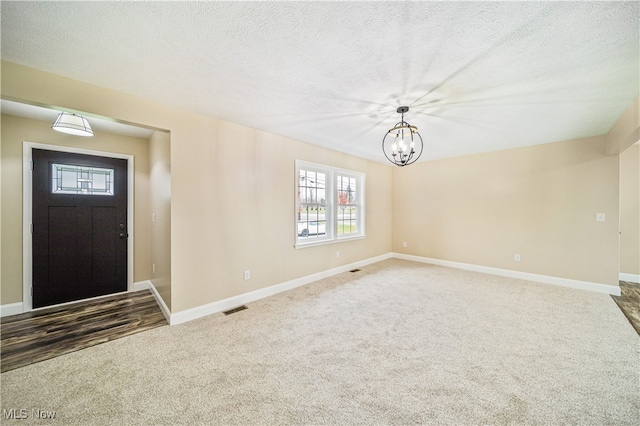 entryway with a textured ceiling, an inviting chandelier, and carpet floors