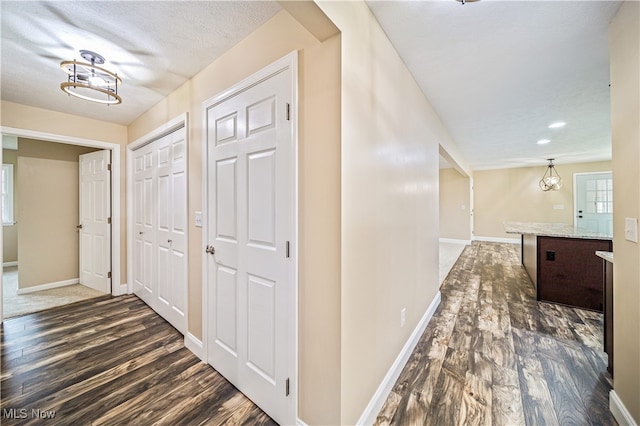 hallway featuring dark wood-type flooring, a textured ceiling, and an inviting chandelier