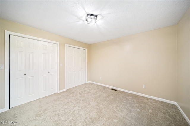 unfurnished bedroom with a textured ceiling, light carpet, and multiple closets