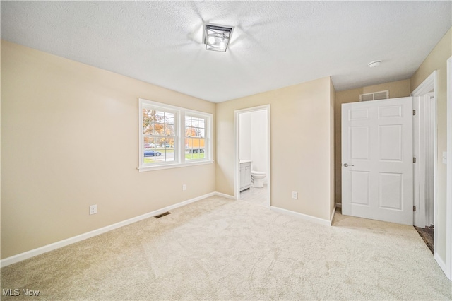 unfurnished bedroom featuring a textured ceiling, light carpet, and ensuite bath