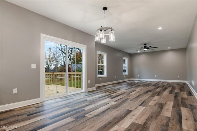 spare room featuring ceiling fan with notable chandelier, wood-type flooring, and a wealth of natural light