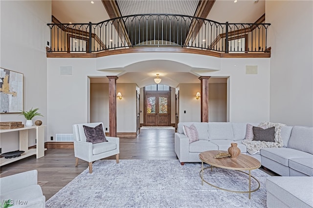 living room featuring hardwood / wood-style flooring, ornate columns, and high vaulted ceiling