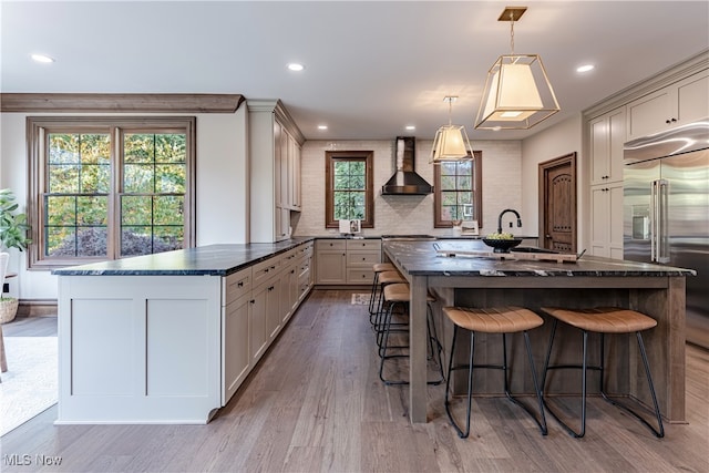 kitchen featuring stainless steel built in fridge, a spacious island, hardwood / wood-style floors, wall chimney range hood, and pendant lighting