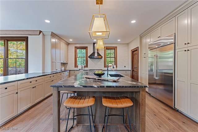 kitchen with pendant lighting, plenty of natural light, wall chimney exhaust hood, and built in refrigerator