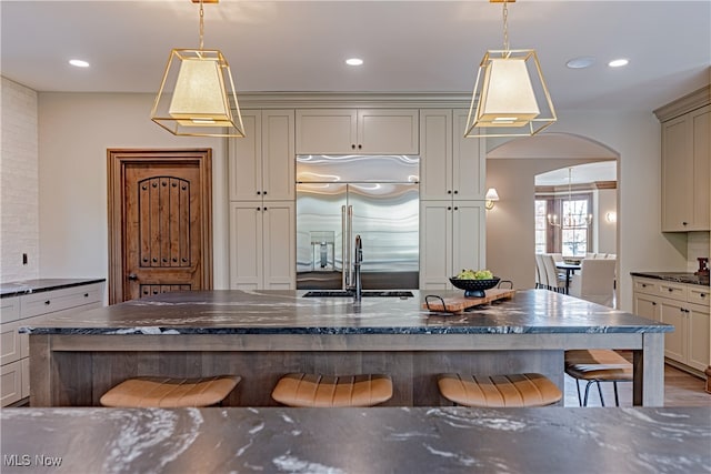 kitchen featuring sink, a kitchen bar, built in fridge, cream cabinetry, and pendant lighting