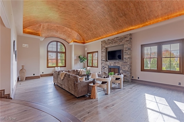 living room with a stone fireplace, light wood-type flooring, and vaulted ceiling