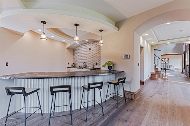 kitchen featuring hardwood / wood-style floors, kitchen peninsula, decorative light fixtures, and a breakfast bar