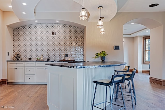 kitchen with light hardwood / wood-style floors, sink, backsplash, hanging light fixtures, and white cabinets