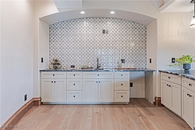 kitchen with decorative backsplash, sink, white cabinetry, light wood-type flooring, and dark stone countertops