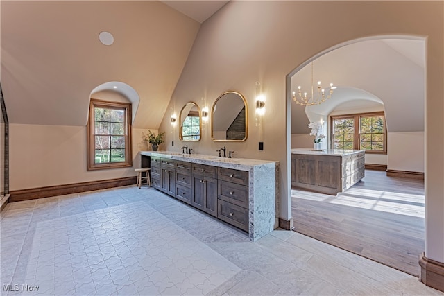 bathroom with a notable chandelier, wood-type flooring, vanity, and vaulted ceiling