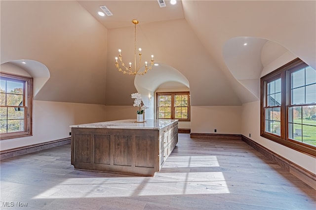 additional living space with high vaulted ceiling, light wood-type flooring, and an inviting chandelier