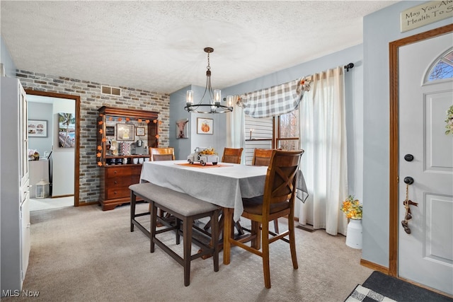 carpeted dining room with brick wall, an inviting chandelier, and a textured ceiling