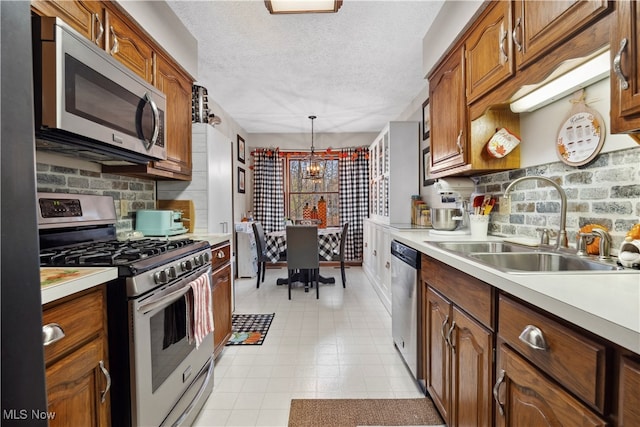 kitchen with sink, appliances with stainless steel finishes, a textured ceiling, a notable chandelier, and pendant lighting