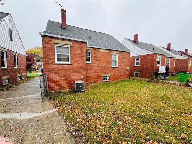 rear view of property with central AC unit and a lawn