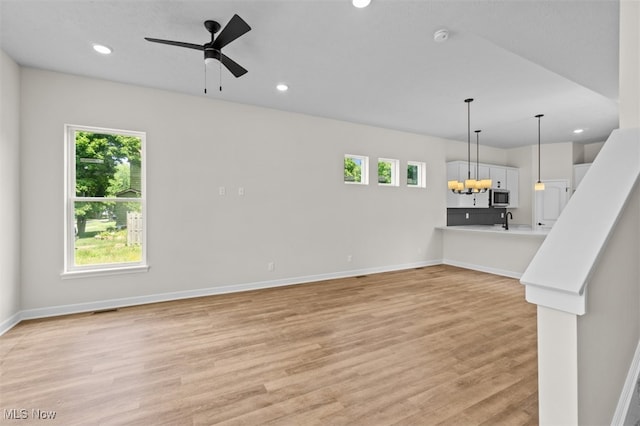 unfurnished living room with ceiling fan with notable chandelier, light hardwood / wood-style floors, and sink