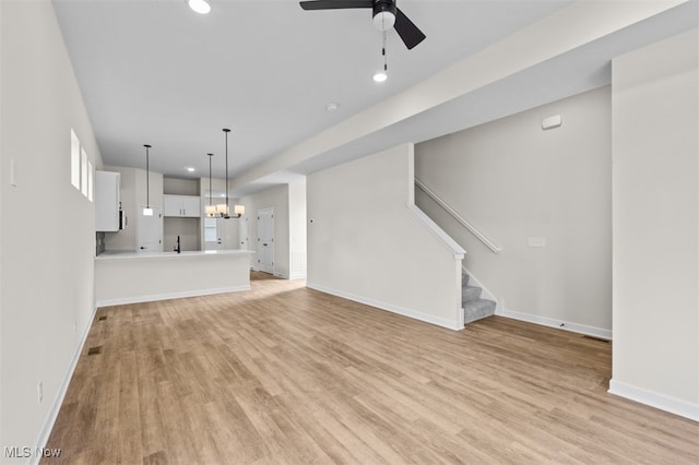 unfurnished living room with ceiling fan with notable chandelier and light hardwood / wood-style flooring