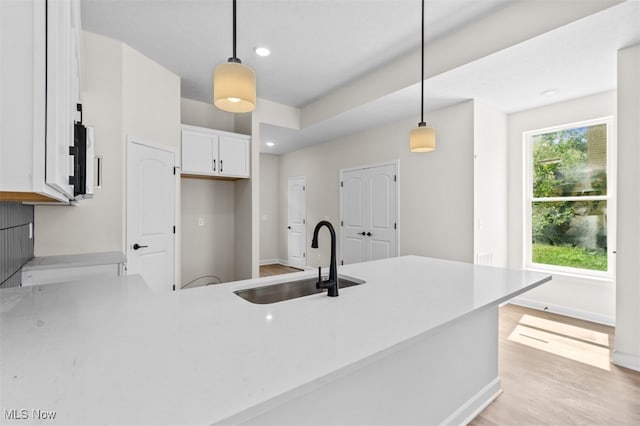 kitchen featuring light hardwood / wood-style floors, kitchen peninsula, sink, white cabinetry, and decorative light fixtures