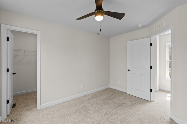 unfurnished bedroom with a closet, a spacious closet, light colored carpet, and ceiling fan