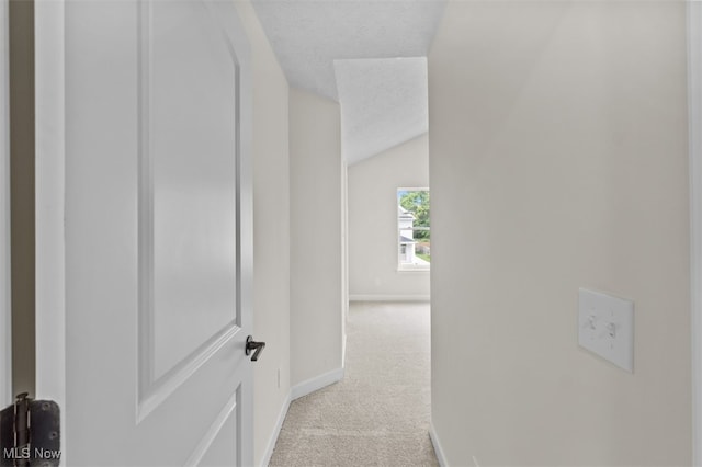 hallway featuring a textured ceiling, light carpet, and vaulted ceiling