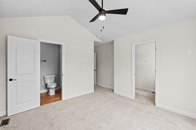 unfurnished bedroom featuring a closet, a walk in closet, vaulted ceiling, ceiling fan, and ensuite bathroom