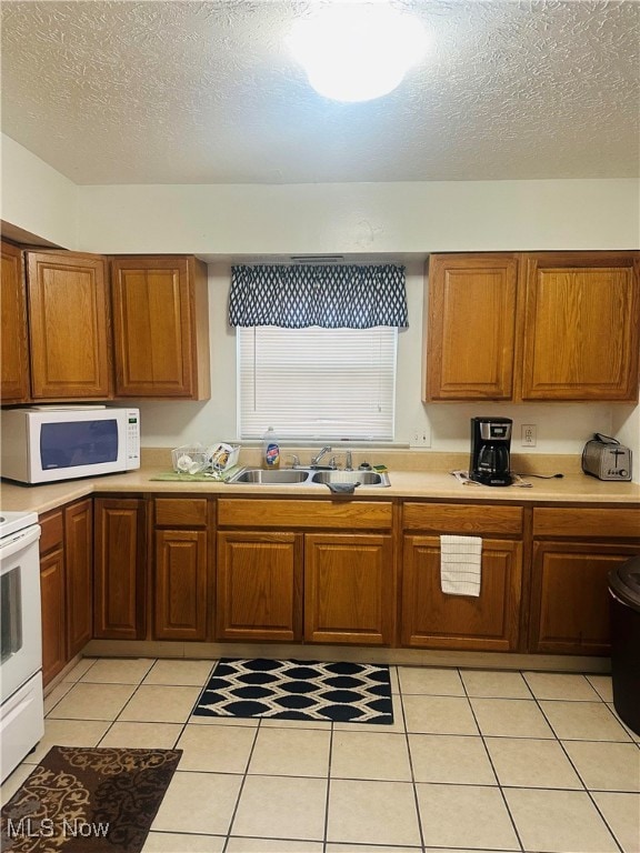 kitchen featuring white appliances, a textured ceiling, light tile patterned floors, and sink