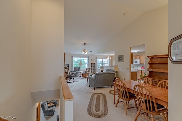 carpeted dining area featuring ceiling fan with notable chandelier and high vaulted ceiling