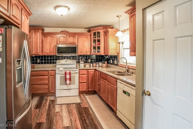 kitchen with sink, appliances with stainless steel finishes, light stone countertops, decorative light fixtures, and dark wood-type flooring