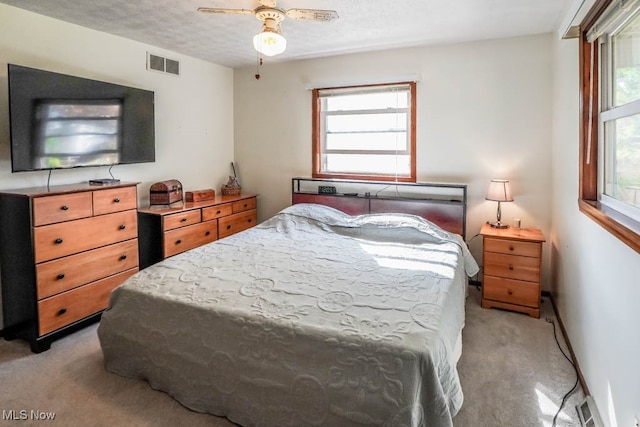 carpeted bedroom featuring ceiling fan, multiple windows, and a textured ceiling