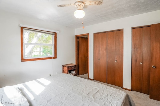 bedroom with two closets, light colored carpet, ceiling fan, and a textured ceiling